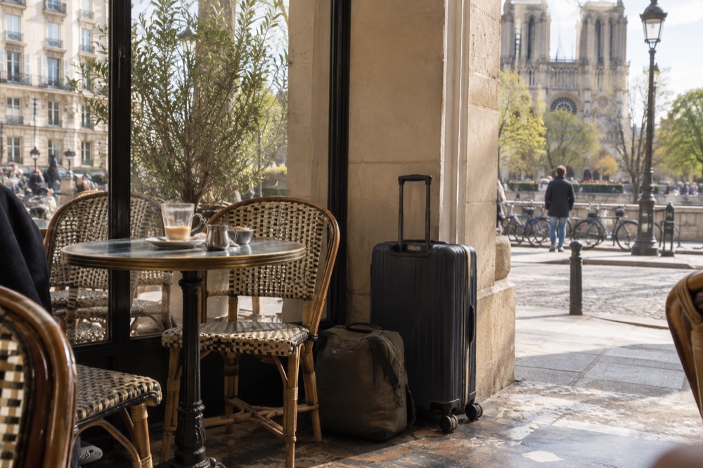 A suitcase standing closed beside a day bag on the floor of a bright Paris café
