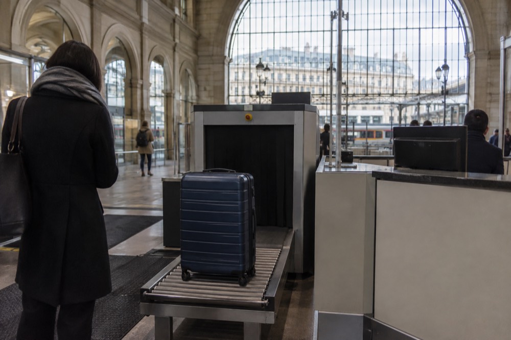A suitcase beside security screening equipment at an airport service counter near Paris