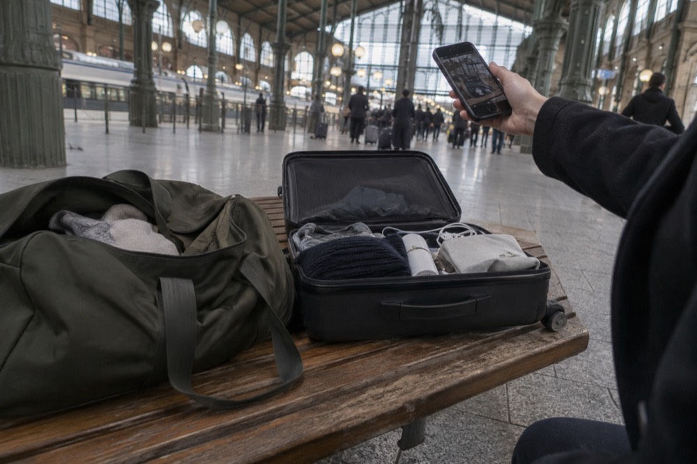 Suitcase open on a bench with a phone photographing the contents