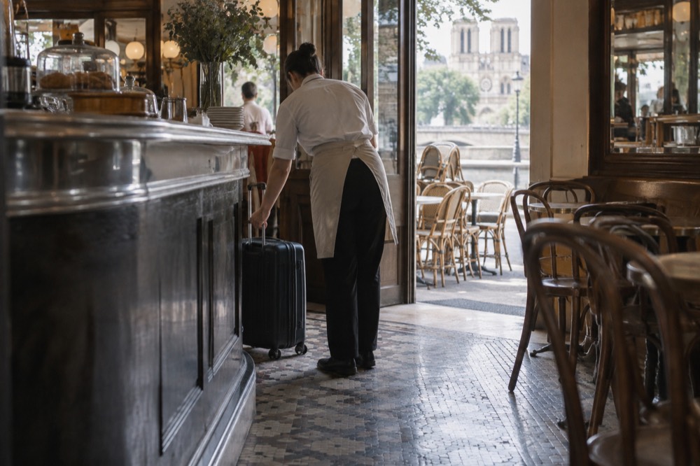 A café counter in Paris where a staff member receives a suitcase for storage