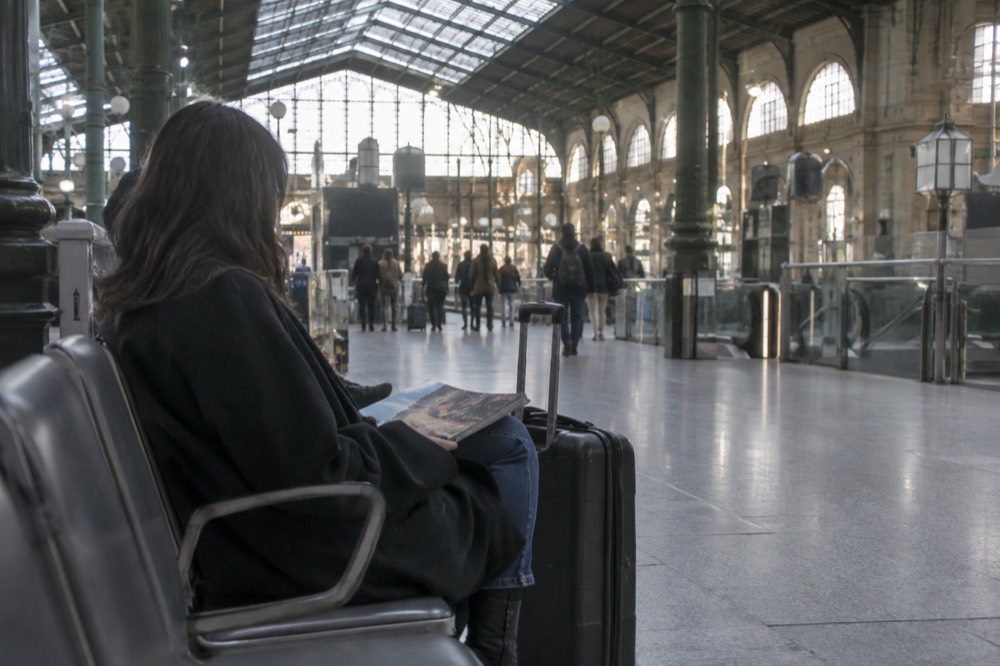 A traveller waiting in an airport terminal with a suitcase beside a row of seats
