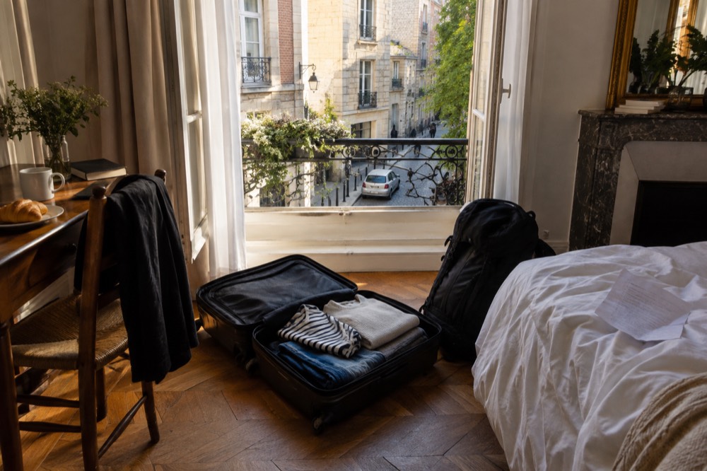 An open suitcase on a hotel room floor with a packed bag beside it at checkout time