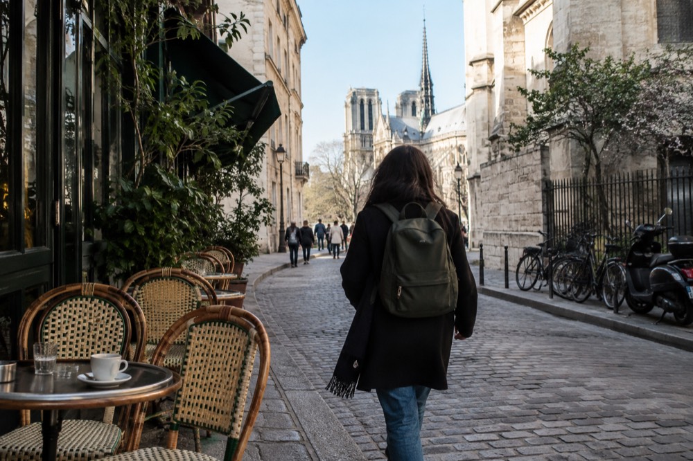 A traveller with a small rucksack passing cafe terraces on a Paris street on a clear afternoon