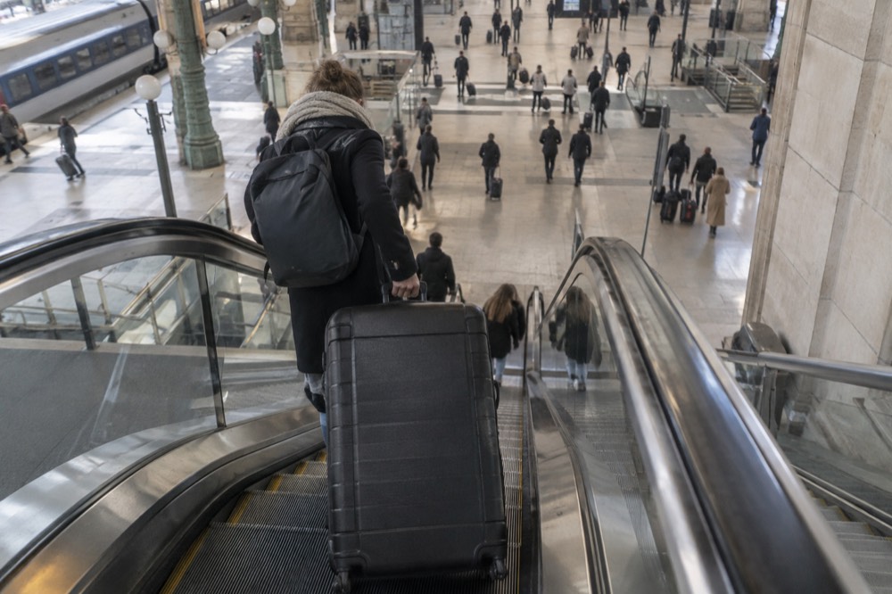 A traveller easing a suitcase onto an escalator down to a lower station level in Paris