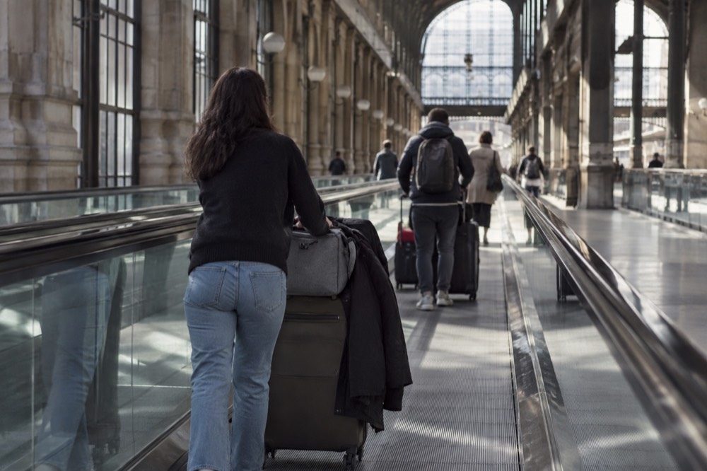 Travellers with trolleys of luggage on a moving walkway in an airport corridor near Paris