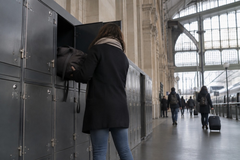 Traveler placing a suitcase into a large metal station locker