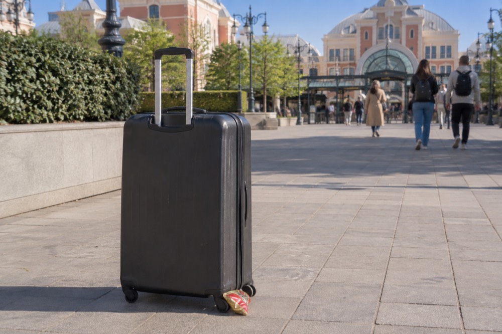 A large suitcase standing beside a themed park entrance arch under a clear sky