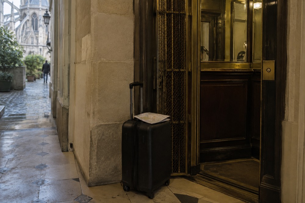 A suitcase standing beside a hotel lift in a narrow Paris corridor