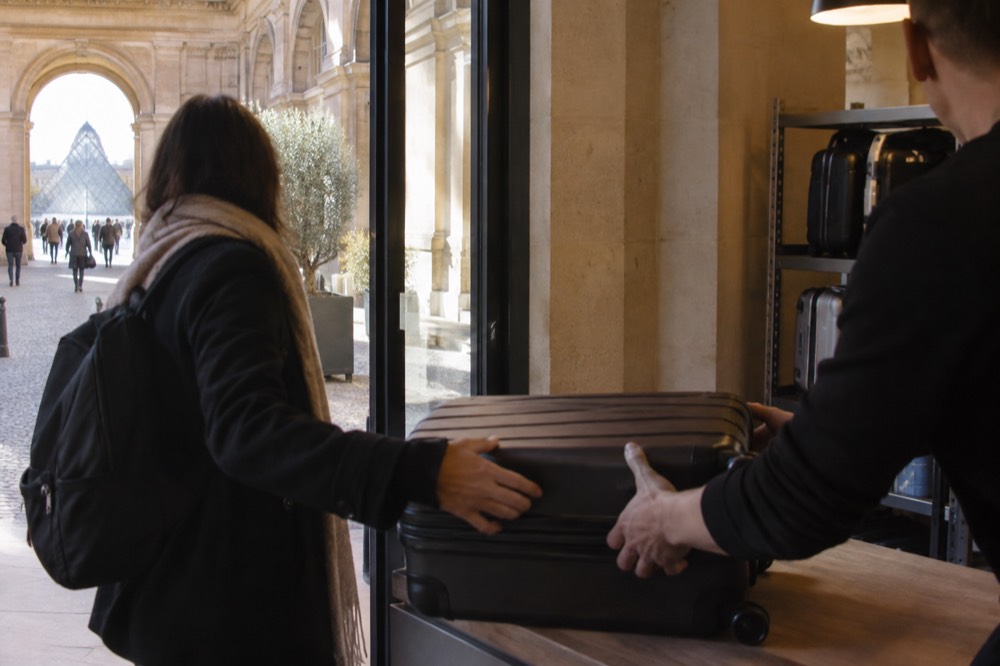 Traveller handing a suitcase across a shop counter at a city storage point