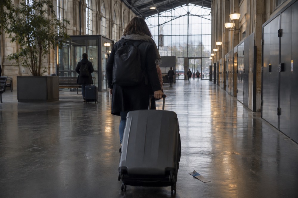 A traveller wheeling a suitcase along an airport terminal corridor near Paris