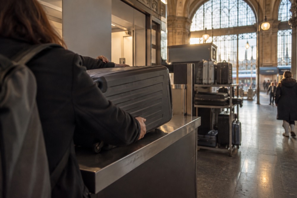 A traveller handing a suitcase to a staff member at a luggage storage counter inside a station