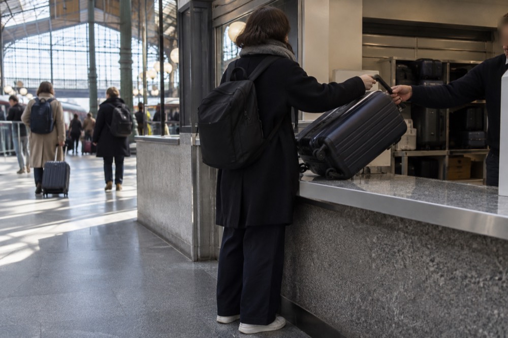 A staffed left-luggage counter window in a railway station, with a suitcase being handed over