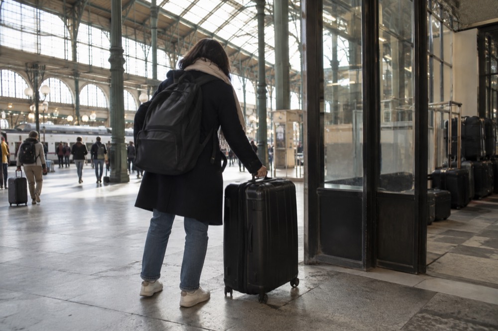 A traveller setting a suitcase down inside a bright Paris railway station concourse