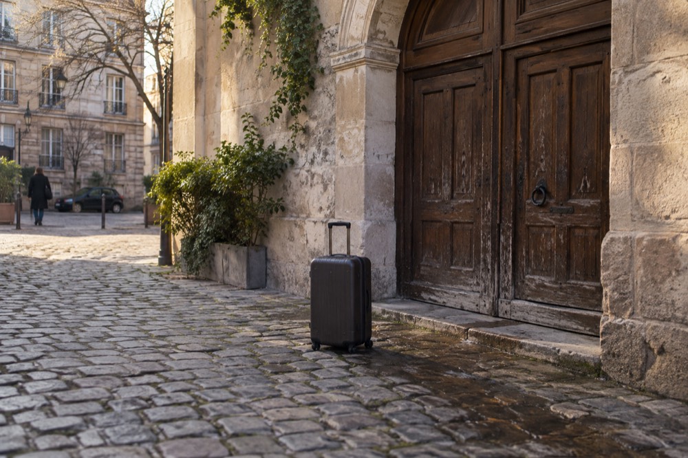 A suitcase outside the closed wooden door of a small Paris hotel with a stone facade