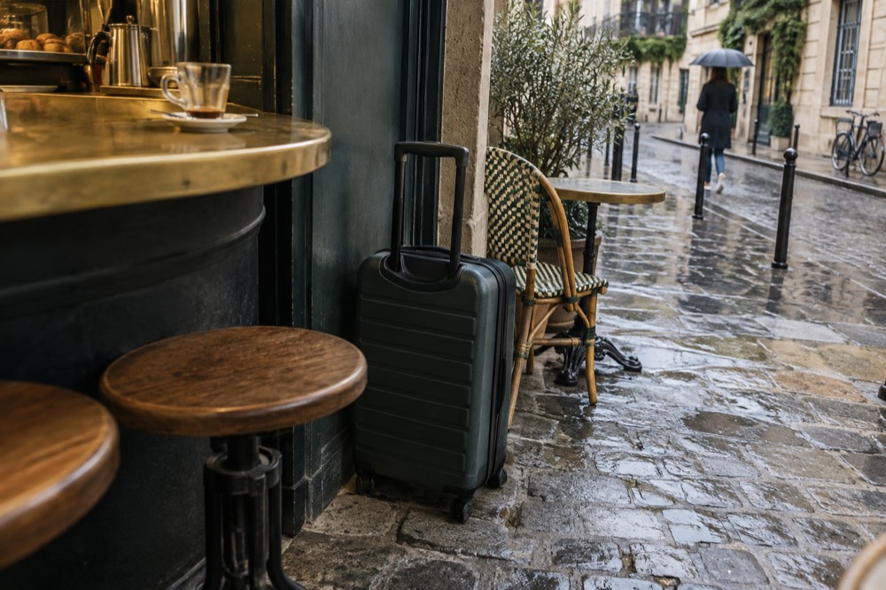 Suitcase parked beside a cafe counter in Paris with a shopkeeper's till in the background