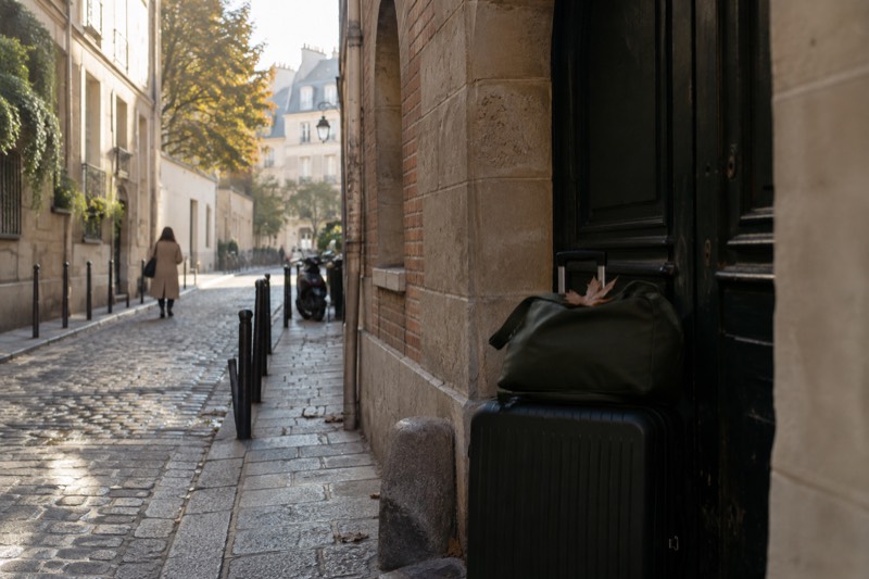Two bags stacked in an arched carriage doorway off a cobbled lane in Le Marais, one of the central Paris districts where shops and hotels hold luggage for a fee per bag per day.