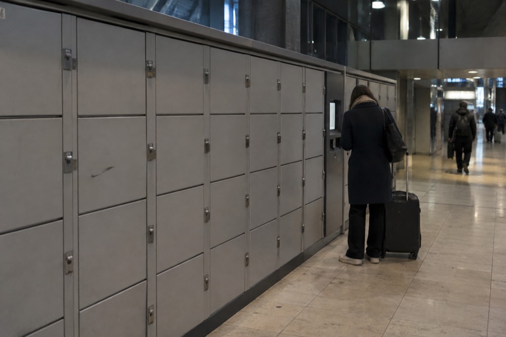 A row of grey self-service lockers in a station corridor with a payment terminal