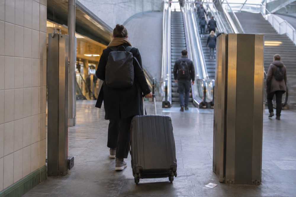 A traveller wheeling a large case through a wide luggage gate onto a Paris metro platform