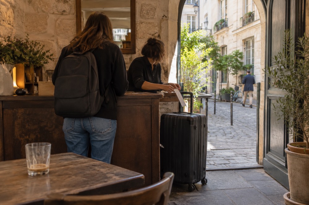 A bright cafe interior with a staffed counter where a suitcase is being handed over and tagged behind the bar