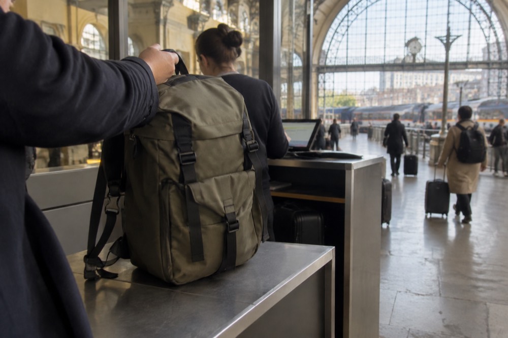 A shop worker accepting a suitcase at a Paris luggage storage point with a booking tablet