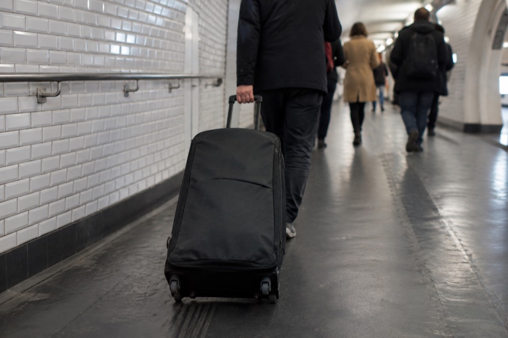 A traveller wheeling a large case along a wide tiled Metro corridor in Paris