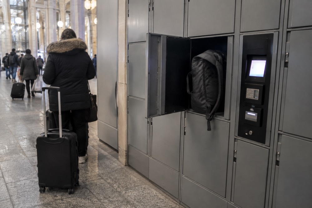 A row of self-service luggage lockers in a station corridor with a payment terminal beside them.