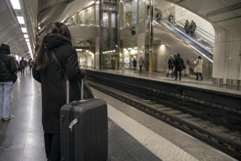 Metro platform with a passenger standing beside a large suitcase waiting for a train