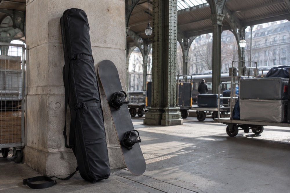 A padded ski bag and a snowboard leaning against a wall inside a storage area