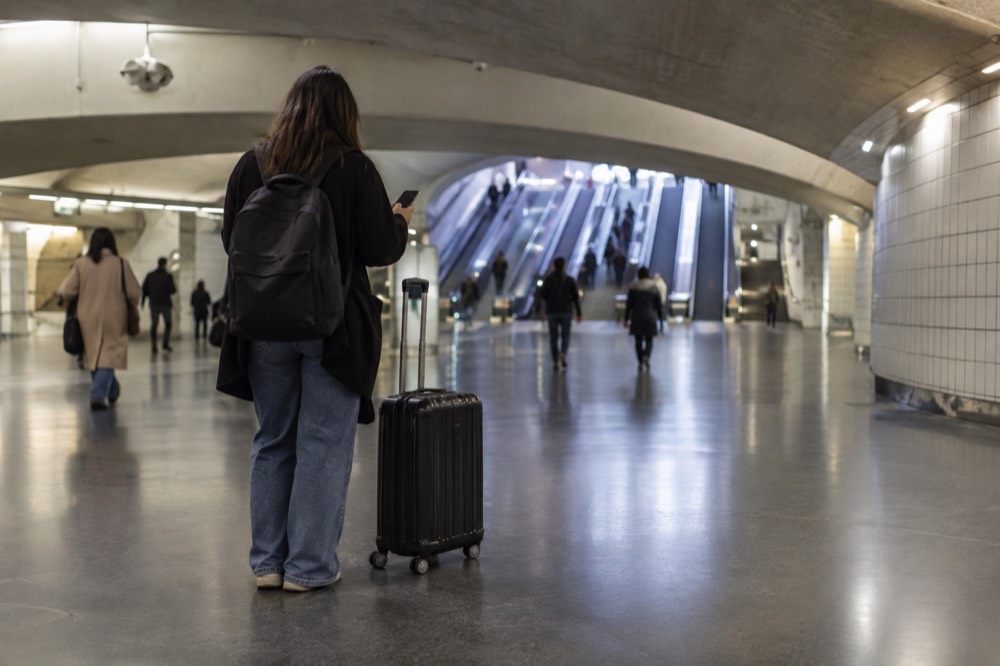 A traveller holding a phone beside a suitcase in a Paris station concourse