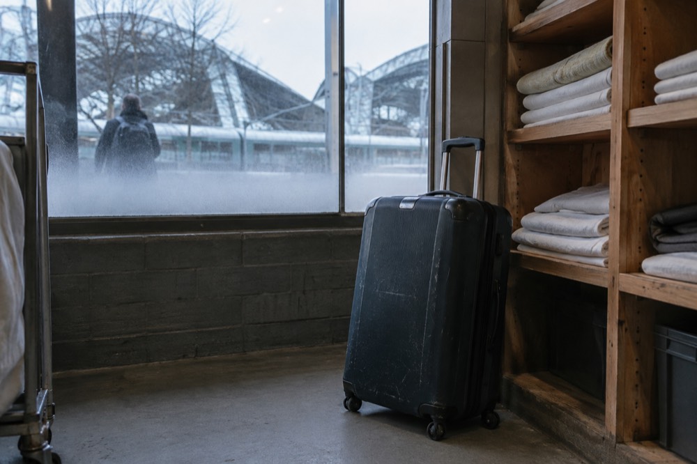 A suitcase parked inside a hotel luggage room beside shelves holding folded items
