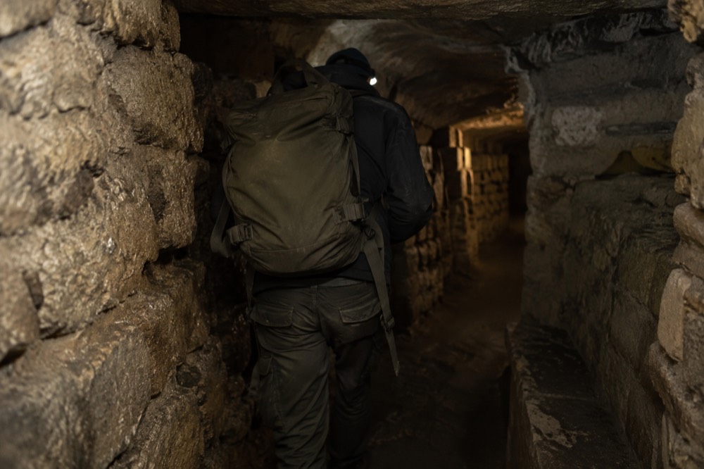 A daypack carried through a narrow stone tunnel in the Paris Catacombs