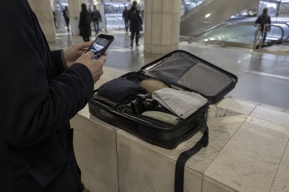 An open suitcase being photographed with a phone before check-in.