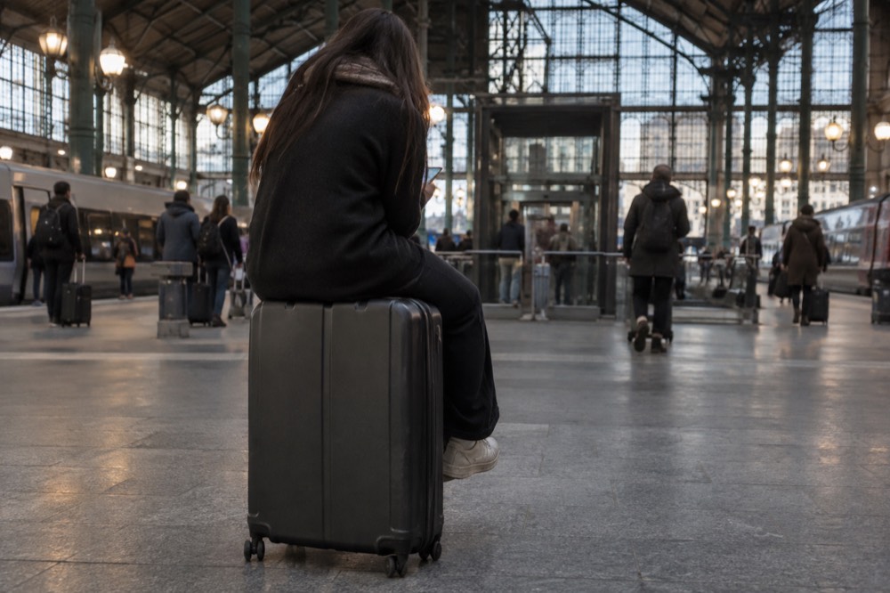 A traveller sitting on a suitcase in a Paris station holding a phone