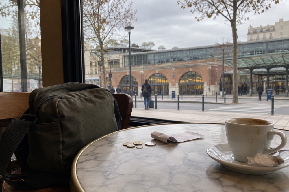 A receipt and euro coins on a cafe table beside a small day bag